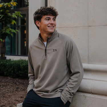 College-aged man wearing the Mushroom Cutter & Buck Adapt quarter-zip with black embroidered Sigma Nu Greek letters outdoors on campus.