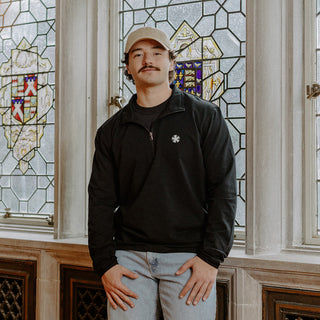 Male model wearing the black Sigma Nu Embroidered Luxe Quarter Zip in front of stained glass windows with fraternity Symbols.