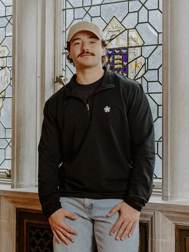Male model wearing the black Sigma Nu Embroidered Luxe Quarter Zip in front of stained glass windows with fraternity Symbols.
