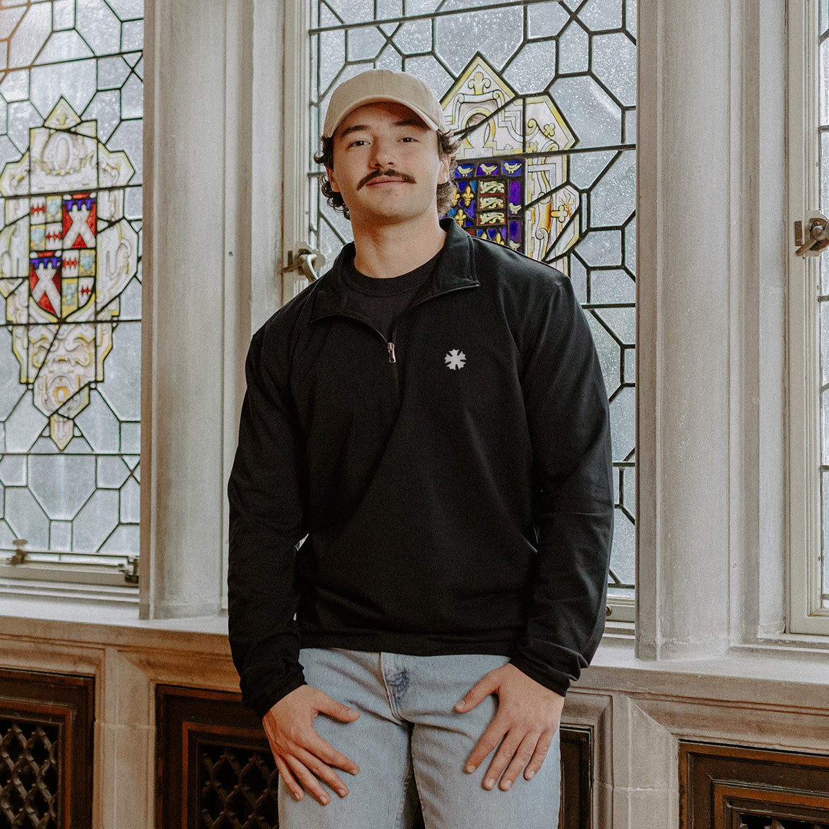 Male model wearing the black Sigma Nu Embroidered Luxe Quarter Zip in front of stained glass windows with fraternity crests.