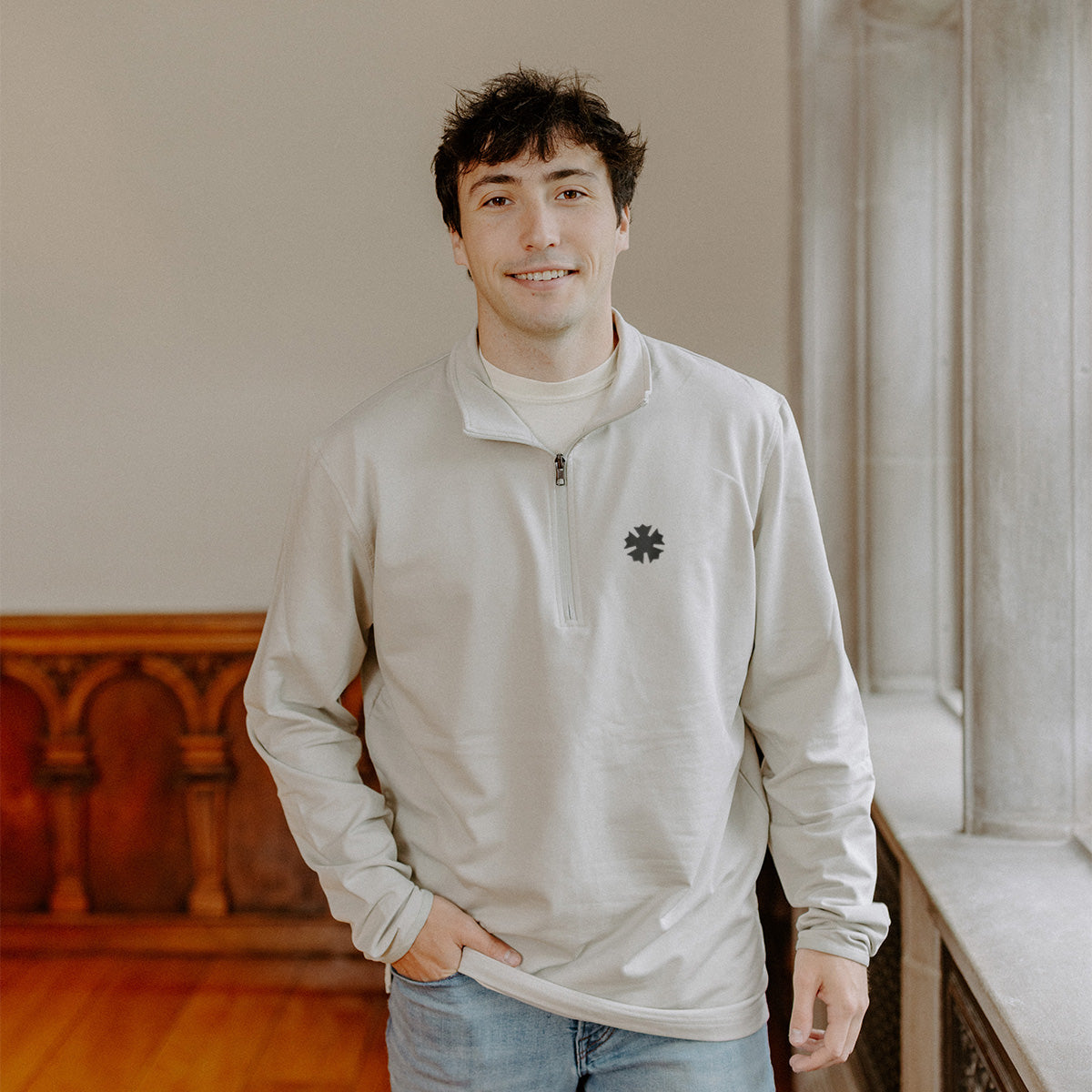 Male model wearing the smoke-colored Sigma Nu Embroidered Luxe Quarter Zip with crest embroidery, standing by a window in a formal setting.