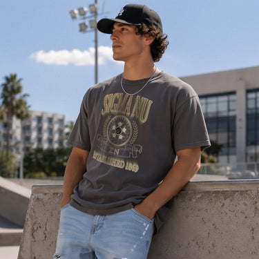 College-aged male wearing the fraternity Collegiate Crest Graphic Tee in charcoal grey, featuring vintage Sigma Nu crest artwork on campus.