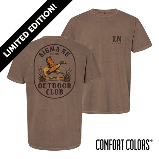 Brown garment-dyed short-sleeve tee featuring a vintage-inspired graphic: a weathered oval frames a mallard in mid-flight with burnt orange and mossy green-tipped wings above rippling water and cattails; distressed Sigma Nu arcs overhead and Sigma Nu letters bold and rugged on the front.